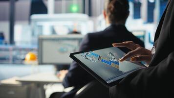 Photovoltaics specialist designs production lines in CAD app using tablet. Solar panels plant technician uses simulation software on device to optimize production layouts, camera A closeup photo