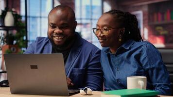 Couple using ear buds to listen to podcast or attend webinar, hearing online discussion on web platform. Self employed man and woman spend time at desk. Camera B. photo