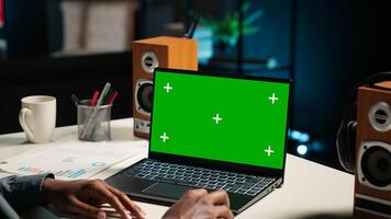 African american man working from home with green screen on laptop, looking at data on web. Remote worker in personal apartment office crosschecking important info. Camera B. photo