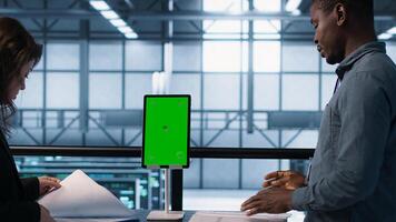 Inspector checking documents in server hub to ensure compliance with industry standards, using mockup tablet. Admin team inspecting files, overseeing data center security protocols, camera A photo