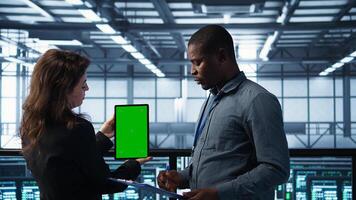 Engineers using green screen tablet, checking infrastructure reliability and writing on clipboard. Workers using mockup device in server room, managing virtualization, camera B photo