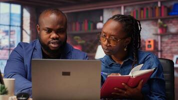 Remote employees organizing calendar appointments using laptop and ledger, checking papers and synchronizing important tasks on schedule. Man and woman review files at home. Camera B. photo