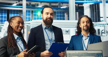 Portrait of inspectors in photovoltaics factory reviewing performance of robot arms placing solar panels on assembly lines. Team of happy supervisors inspecting machinery, camera B photo