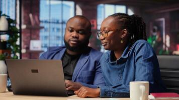 Black freelancers at home desk using laptop and checking emails, reading messages in inbox and solving daily tasks. Couple managing electronic correspondence. Camera B. photo
