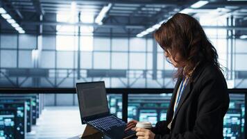 Technician using laptop in data center, finetuning network protocols and holding coffee cup. Woman in server room coding on notebook, enforcing advanced security measures, camera B photo