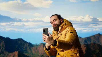 Determined adventurer enjoys panoramic mountain landscape, taking selfies with amazing scenic background on hill top where nature and towering peaks create breathtaking view. Camera B. photo