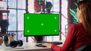 Adult woman typing on pc with chroma key screen at loft desk, engaging in online work, multitasking efficiently and embracing flexibility of remote tasks in home setting. Camera A. photo