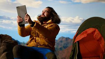 Reckless explorer struggling with wind and weak internet connection, camping on scenic rocky mountain peak. Hiker in danger with extreme cold weather. Camera B. photo