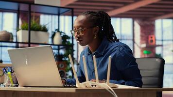 Black woman at home examines modem and troubleshooting guide book, struggling to fix WiFi router and restore internet connection for remote freelance tasks. Signal loss. Camera B. photo