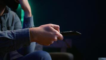 Close up of man on couch browsing through movies available on streaming service. Focus on remote control used by homeowner in apartment switching channels on TV, camera B photo