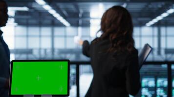 Focus on chroma key device in front of technicians analyzing metrics. Close up of isolated screen tablet next to server hub workers ensuring seamless operations, camera B photo