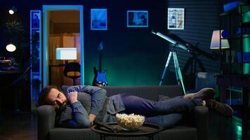 Man hugging pillow and watching TV, heartbroken by upsetting movie plot. Sad viewer laying on couch in RGB illuminated apartment, upset by depressing television show scene, camera B photo