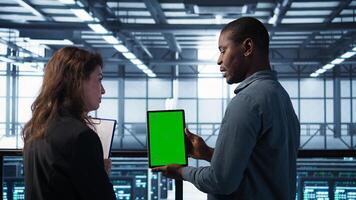 Data scientists using mockup tablet, conducting security audits to prevent bugs. African american man with colleague in data center looking at green screen device, camera B photo