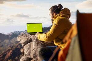 Young traveler embracing high altitude wilderness next to chroma key, using device where the crisp air and scenic mountain view provides inspiring setting for trekking and adventure. photo