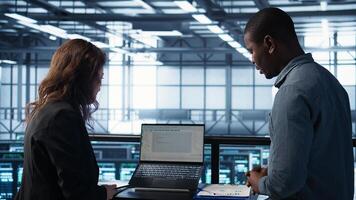 Teamworking data center scientists using artificial intelligence on laptop and tablet. Server room coworkers using neural networks AI on devices to do computing processes, camera B photo