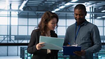 IT professionals in data center reviewing reports and files, crosschecking network performance metrics and security logs. Server room workers troubleshooting systems to prevent downtime, camera A photo