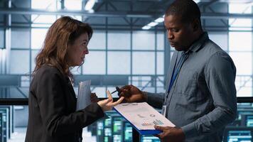 Data center team examining paperwork files and reviewing system diagnostics. Server room workers looking over maintenance schedules and cybersecurity protocols, camera A photo