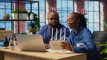 African American couple at home office troubleshooting WiFi modem and discussing solutions to fix weak connection affecting remote work productivity. Router guide files. Camera A. photo