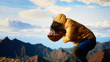 Clumsy traveler loses balance on steep mountain peak as powerful winds knock him off course, falling and being unequipped in expedition. Hiker unprepared for cold weather. Camera B. photo