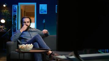 Man at home watching interesting movie on streaming service, enjoying time off from work. Person on couch enjoying high quality film on TV in apartment, camera B photo