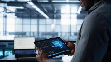 Close up of computer scientist in data center uses AI on tablet, verifying compliance of racks. IT expert using artificial intelligence to optimize resource utilization, camera B photo