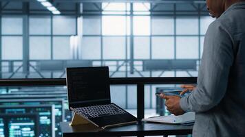 Admin using artificial intelligence tech on tablet and laptop. Man in server farm using AI on devices to update storage arrays, improving performance, camera A photo