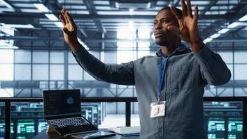 Computer scientist looking at holograms in data center. African american admin interacting with augmented reality AI visualization in server hub, camera B photo