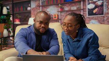 African american people on sofa discussing freelance strategy, researching marketing trends and online data from analytics tools to create growth report. Remote efficiency. Camera A. photo
