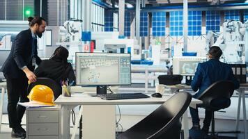 Factory manager walking to employees desks to give tasks after visualizing solar cells designs with 3D software tools, shaping facility floor according to computer simulations photo