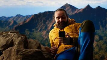 Traveler in warm clothing scrolling social media on top of mountain peak, person always connected with strong signal and obsessed with technology. Climbing hills. Camera B. photo