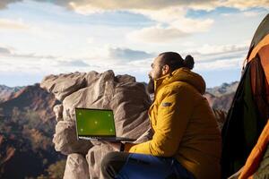 Young traveler embracing high altitude wilderness next to chroma key, using device where crisp air and scenic mountain view provide inspiring setting for trekking and adventure. photo