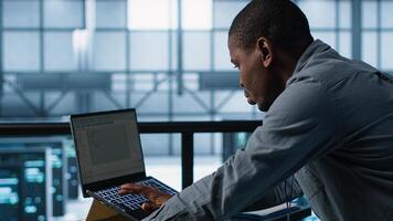 Technician using laptop, adjusting power management settings, using programming languages. Man in server room optimizes resource utilization, maintaining stable infrastructure, camera A photo