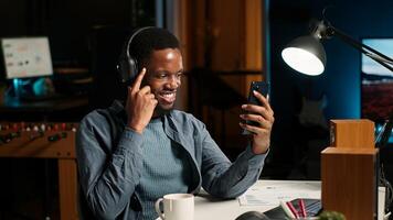 African american man waving and attending web meeting from urban apartment. Engaged male freelancer discussing work remotely with coworkers using phone for videoconferencing. Camera B. photo
