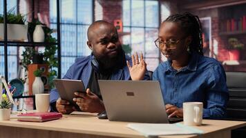 Black woman working while partner listens to music, enjoying time at home together. Female freelancer solving daily tasks on laptop, boyfriend scrolling web. Camera B. photo