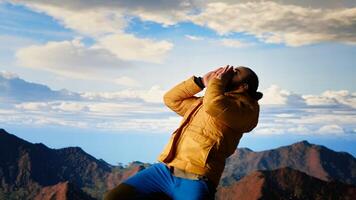 Traveler reaches new heights and doing victory dance on mountain top, feeling satisfaction and motivation. Breathtaking view of mountain range and sky reflects adventure. Camera B. photo