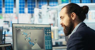 Photovoltaics technician adjusts system parameters on laptop to maximize cells power generation. Man using notebook optimizing energy supply in solar panel manufacturing plant, camera B photo