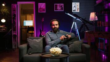 Gamer sitting on couch engaging in online competitive multiplayer game using controller. Upbeat player engaging in fun videogames, enjoying leisure time, camera B photo