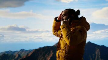 Trekker enjoys high altitude landscape, making phone call, panoramic mountain views and crisp air provides perfect scene for relaxation. Using strong signal on smartphone. Camera B. photo