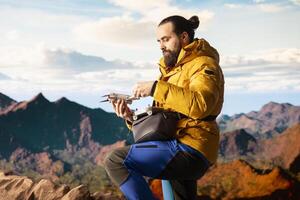 Modern traveler creating content and filming with drone, climbing on top of high altitude mountain range. Hiker enjoying landscape scenery, remote control. photo