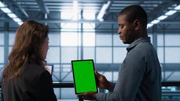 Data scientists using mockup tablet, conducting security audits to prevent bugs. African american man with colleague looking at green screen device, camera A photo