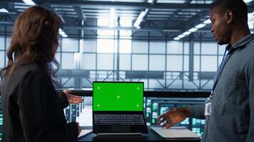 Data center administrators using mockup laptop to review equipment diagnostics. IT specialists adjusting server farm configurations using chroma key notebook photo
