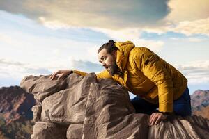 Hiker underestimates mountain peak and getting exhausted at top, slipping on rocks causing accident and risking his life. Young unprepared tired climber losing balance. photo