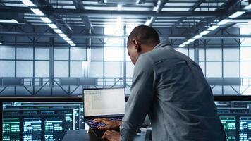Engineer coding on laptop, optimizing resource utilization, adjusting power management settings. Server room worker maintaining stable infrastructure using notebook, camera B photo