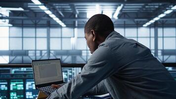 Technician using laptop, adjusting power management settings with programming languages. Man in server room optimizes resource utilization, maintaining stable infrastructure, camera B photo