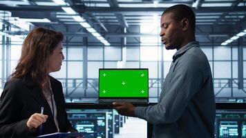 Technicians using green screen mockup laptop to develop disaster recovery plans. IT specialists in server farm testing failover scenarios on chroma key device, protecting data, camera B photo