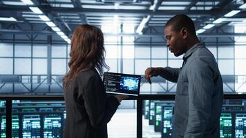 Software developers use AI technology on tablet to optimize storage volumes. IT specialists in server hub facility using artificial intelligence to ensure seamless operations, camera B photo