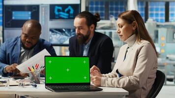 Factory engineers using green screen laptop to refine designs for increased energy output using data. Photovoltaics specialists design solar cell prototypes on chroma key notebook, camera B photo