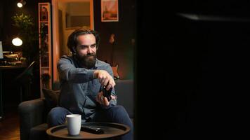 Energetic gamer excited to do gaming during leisure time. Enthusiastic man entering room, jumping on couch, excited to play videogame on console, relaxing after hard day at work, camera B photo