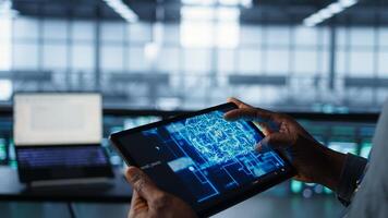 Programmer using AI tech on tablet, testing equipment failover scenarios. Server farm IT specialist uses artificial intelligence on device, ensuring data accessibility, camera B closeup photo