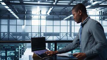 Technician with laptop and tablet integrating AI driven automation tools. Server room worker using artificial intelligence on devices, ensuring continuous uptime, camera B photo
